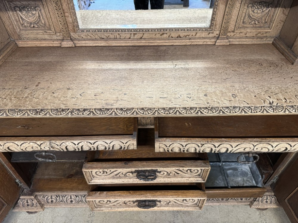 A large carved light oak sideboard with an upper cupboard section, a central mirror plate, turned columns, and detailed relief carvings throughout. View XIII