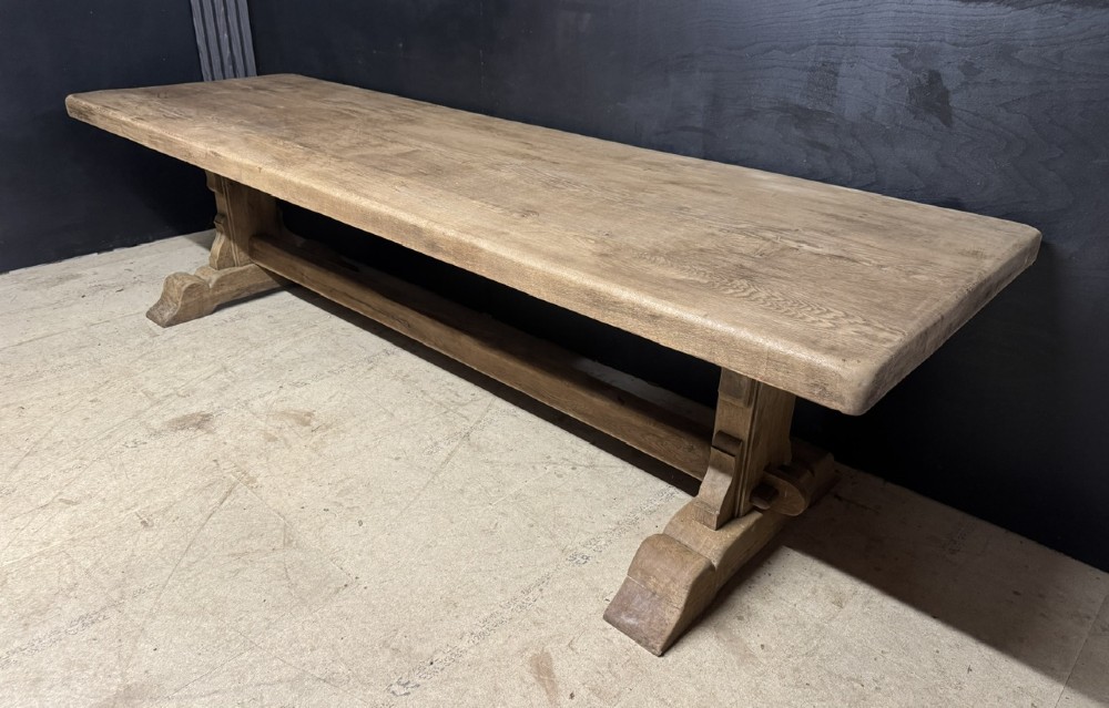 A long French oak trestle dining table featuring a thick wooden top, robust pedestal supports, and a central stretcher with pegged joints.