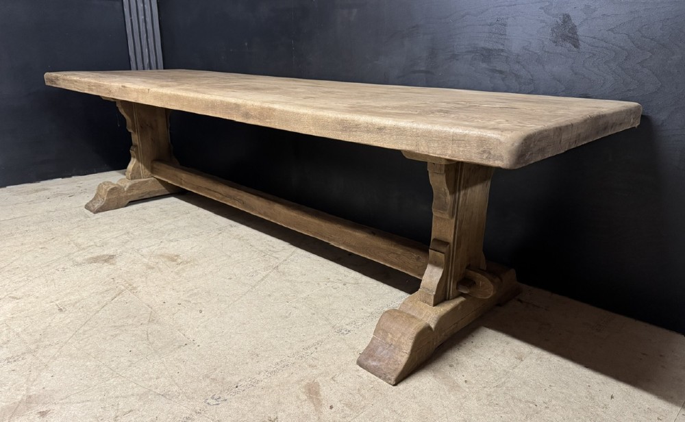 A long French oak trestle dining table featuring a thick wooden top, robust pedestal supports, and a central stretcher with pegged joints. View III