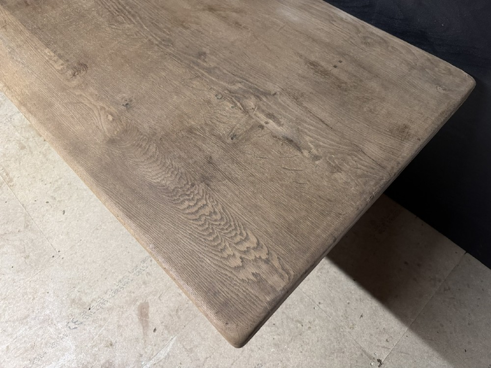 A long French oak trestle dining table featuring a thick wooden top, robust pedestal supports, and a central stretcher with pegged joints. View VI