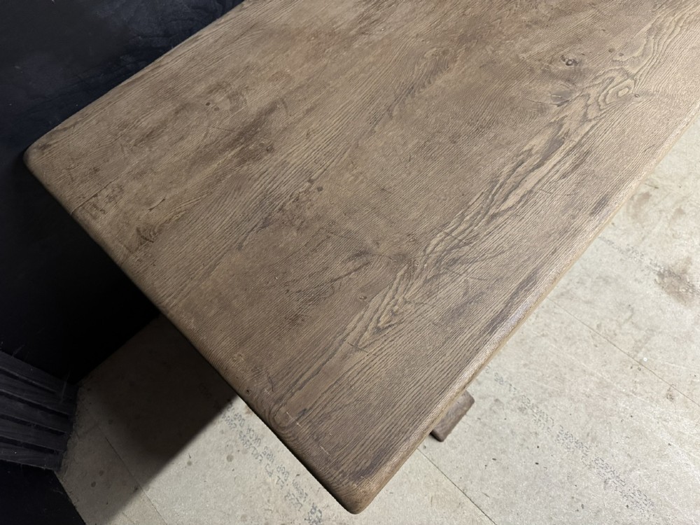 A long French oak trestle dining table featuring a thick wooden top, robust pedestal supports, and a central stretcher with pegged joints. View VII