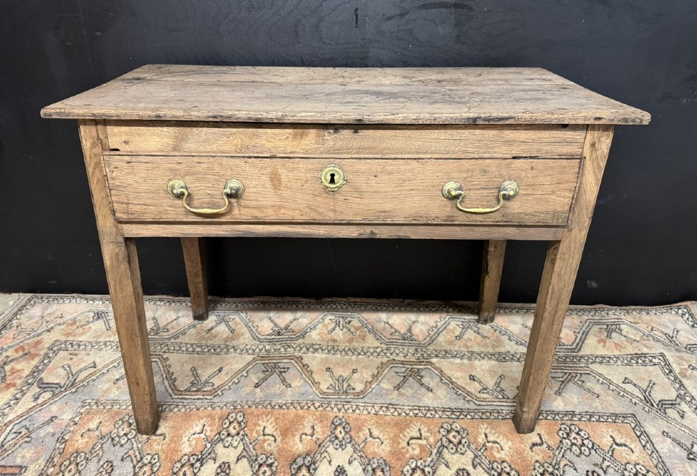 A Georgian natural oak side table with a wide single drawer, two brass swan-neck handles, a brass escutcheon, and four straight square legs.