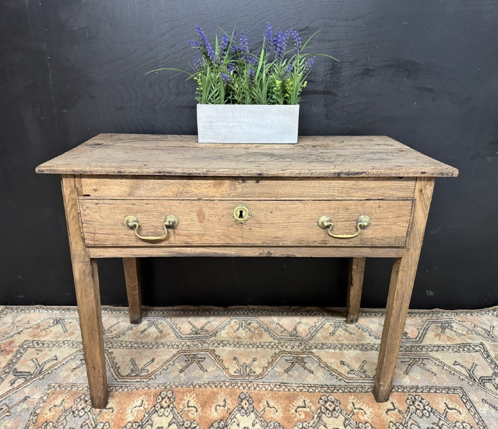 A Georgian natural oak side table with a wide single drawer, two brass swan-neck handles, a brass escutcheon, and four straight square legs. View II