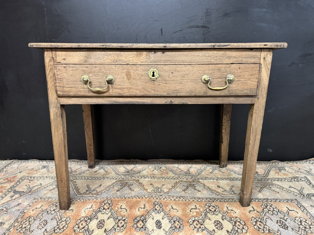 A Georgian natural oak side table with a wide single drawer, two brass swan-neck handles, a brass escutcheon, and four straight square legs. View III