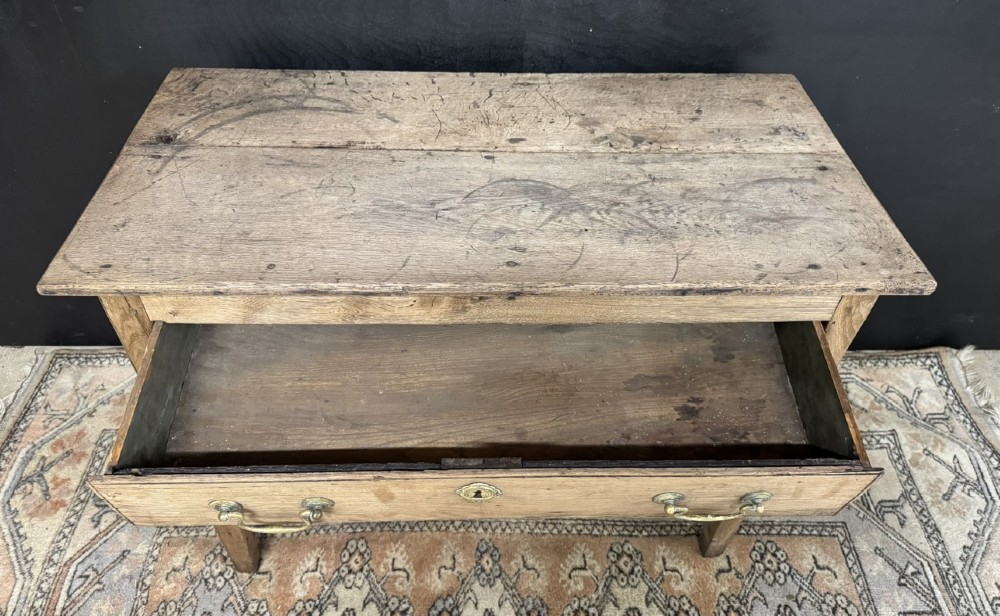A Georgian natural oak side table with a wide single drawer, two brass swan-neck handles, a brass escutcheon, and four straight square legs. View V