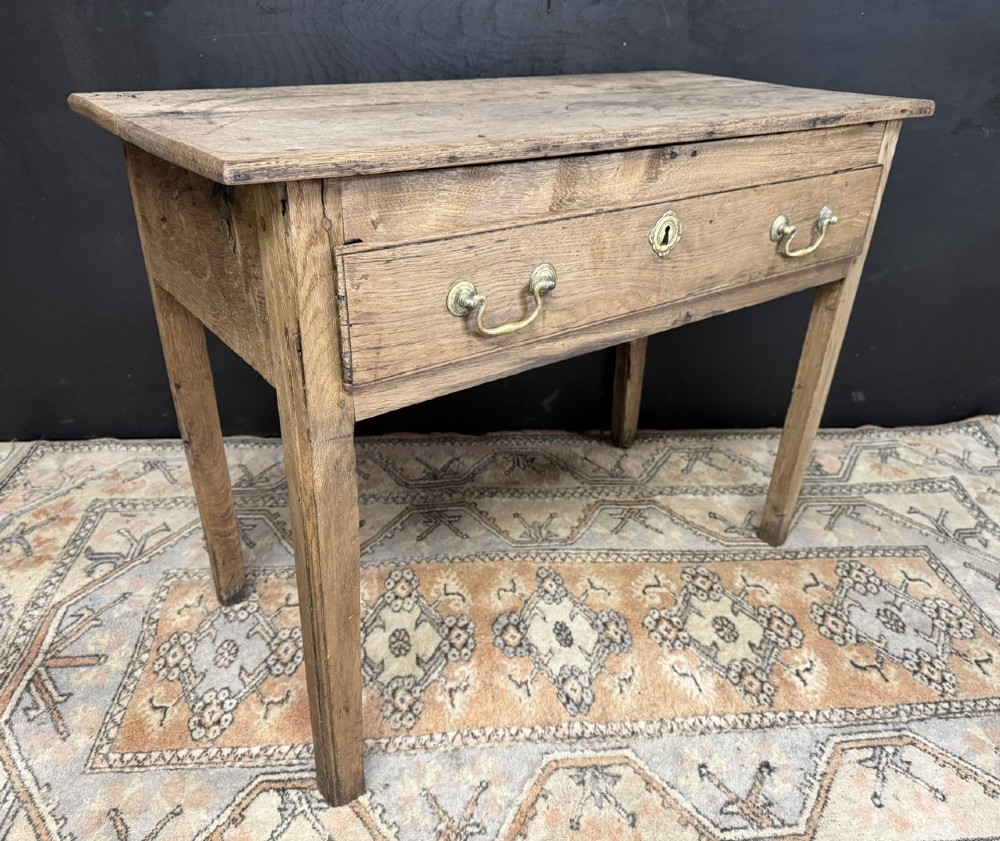 A Georgian natural oak side table with a wide single drawer, two brass swan-neck handles, a brass escutcheon, and four straight square legs. View VI