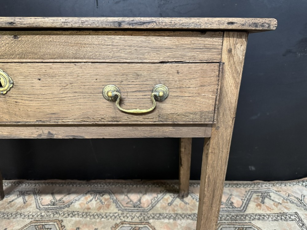 A Georgian natural oak side table with a wide single drawer, two brass swan-neck handles, a brass escutcheon, and four straight square legs. View X