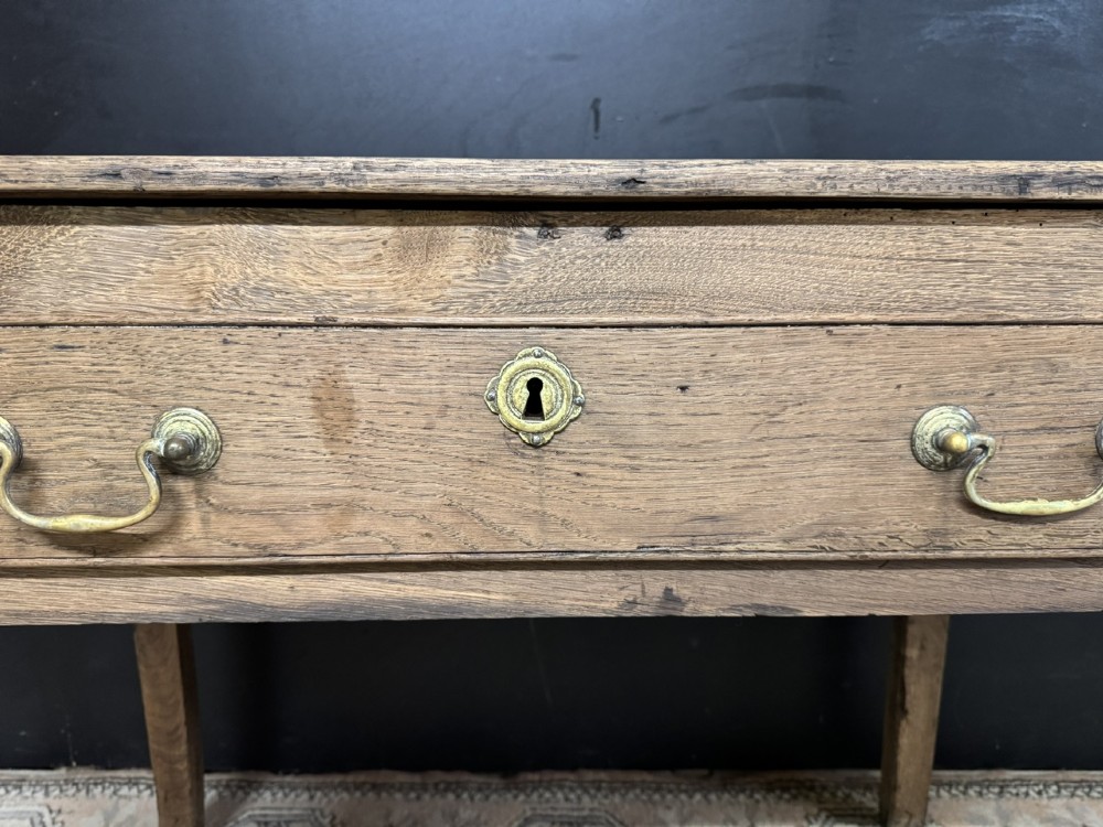 A Georgian natural oak side table with a wide single drawer, two brass swan-neck handles, a brass escutcheon, and four straight square legs. View XI