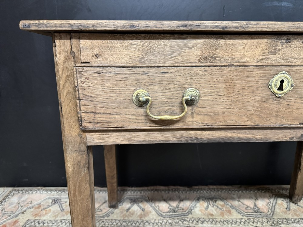 A Georgian natural oak side table with a wide single drawer, two brass swan-neck handles, a brass escutcheon, and four straight square legs. View XII