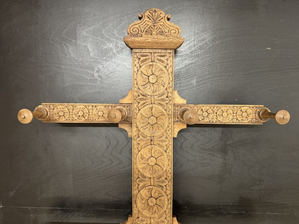 A tall carved oak hall stand featuring two horizontal rails of turned coat pegs, a central column carved with floral rosettes, bobbin-turned legs, and lower umbrella drip trays. View II