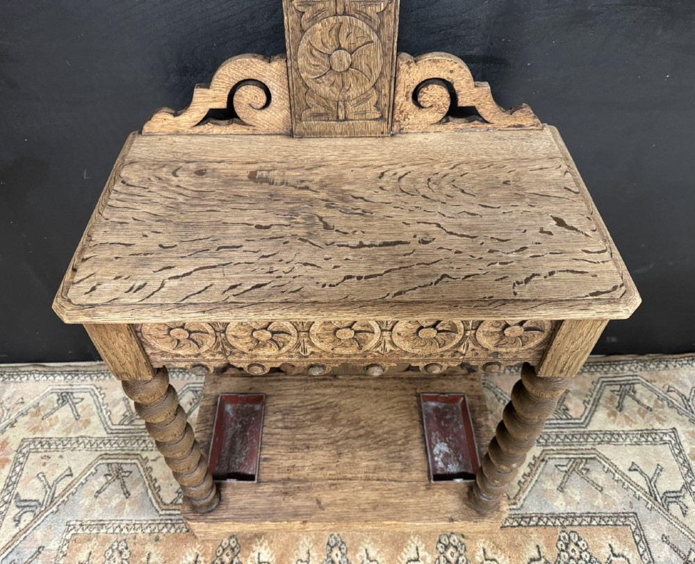 A tall carved oak hall stand featuring two horizontal rails of turned coat pegs, a central column carved with floral rosettes, bobbin-turned legs, and lower umbrella drip trays. View III