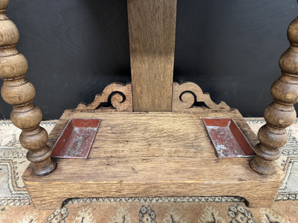 A tall carved oak hall stand featuring two horizontal rails of turned coat pegs, a central column carved with floral rosettes, bobbin-turned legs, and lower umbrella drip trays. View IV