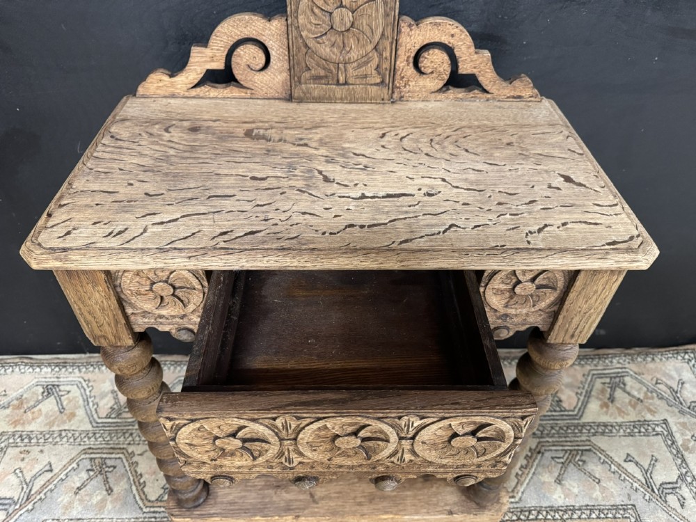 A tall carved oak hall stand featuring two horizontal rails of turned coat pegs, a central column carved with floral rosettes, bobbin-turned legs, and lower umbrella drip trays. View VI