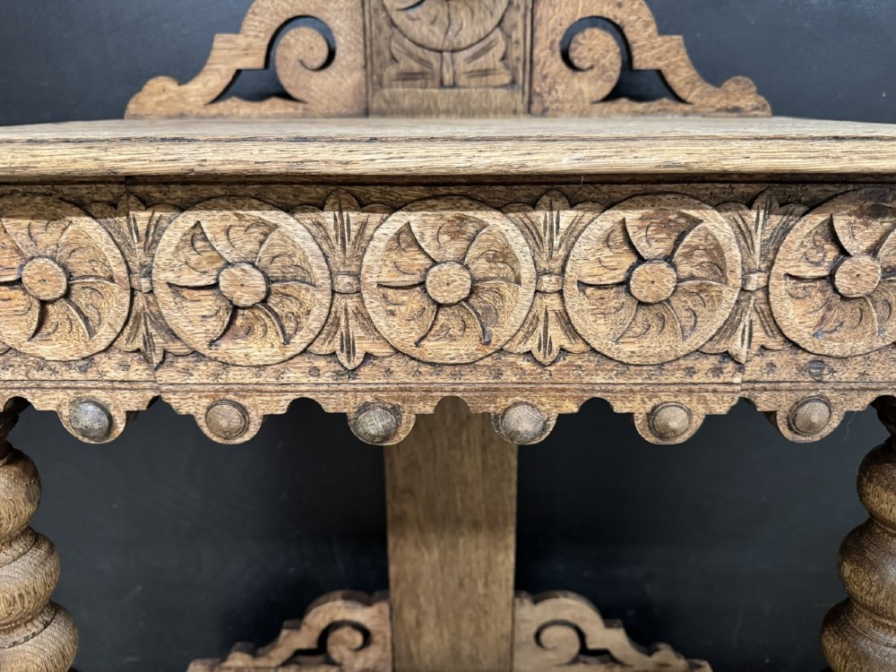 A tall carved oak hall stand featuring two horizontal rails of turned coat pegs, a central column carved with floral rosettes, bobbin-turned legs, and lower umbrella drip trays. View XI