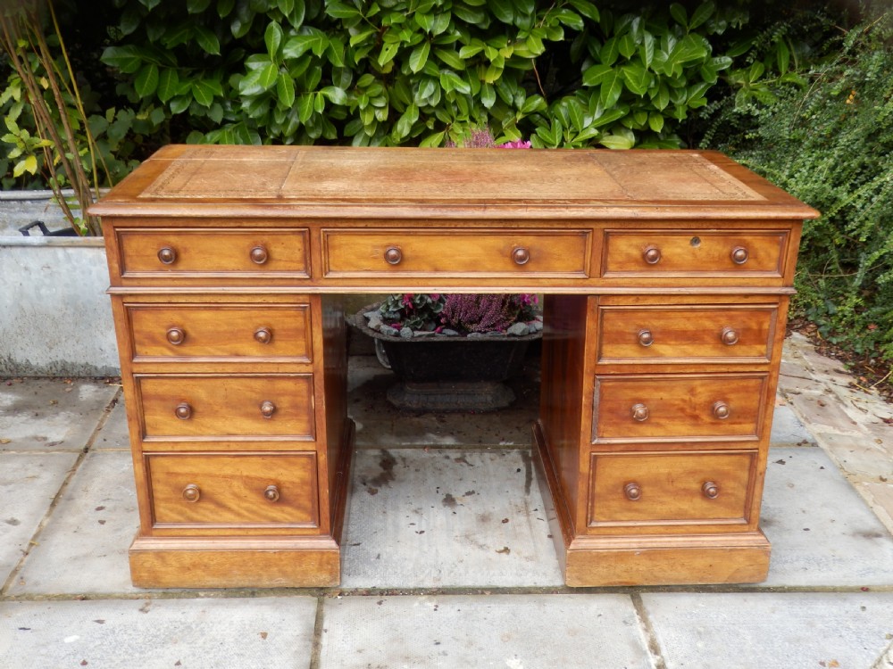 A Victorian warm brown mahogany pedestal desk featuring a gold-tooled leather writing insert and nine drawers with turned wooden knobs on twin plinth bases.