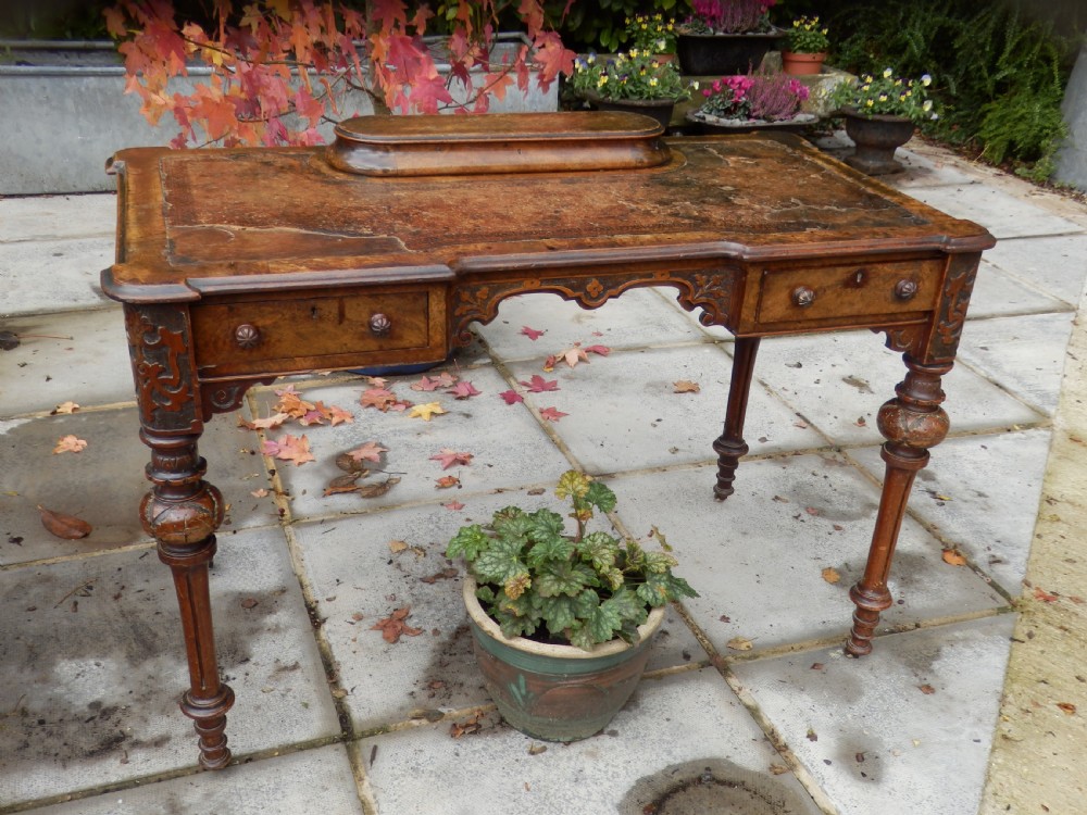 An early Victorian burr walnut writing desk featuring an inset leather writing top, carved frieze drawers, turned legs, and a raised central rear plinth.