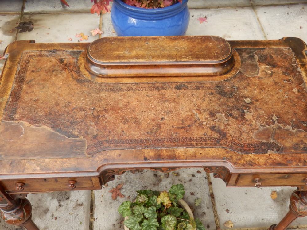 An early Victorian burr walnut writing desk featuring an inset leather writing top, carved frieze drawers, turned legs, and a raised central rear plinth. View III