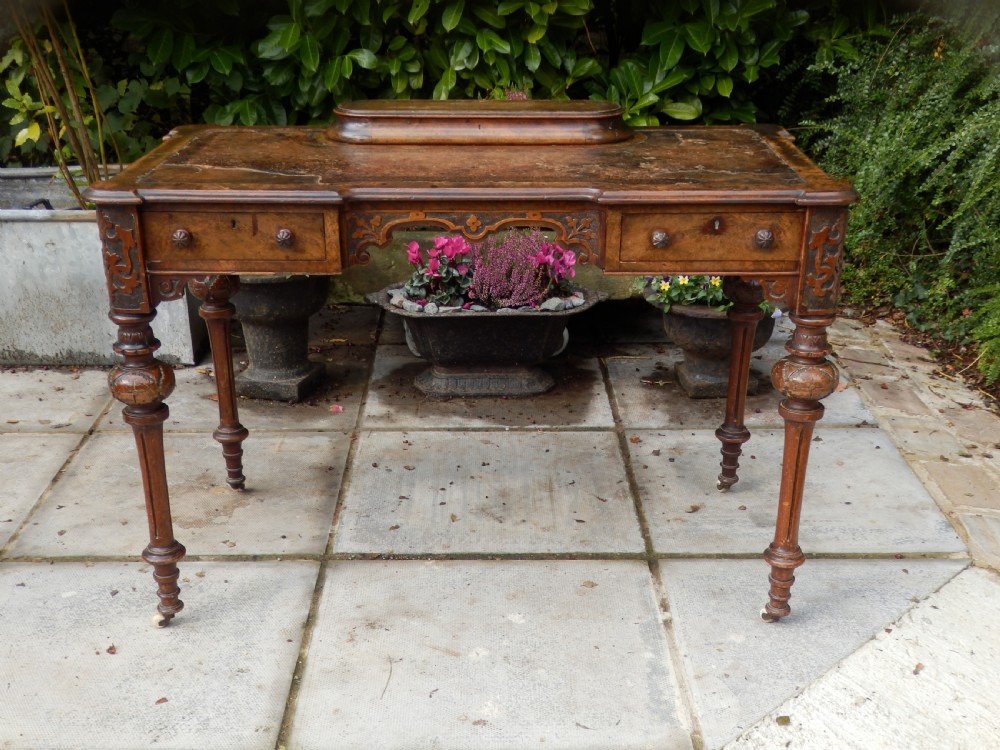 An early Victorian burr walnut writing desk featuring an inset leather writing top, carved frieze drawers, turned legs, and a raised central rear plinth. View XIV