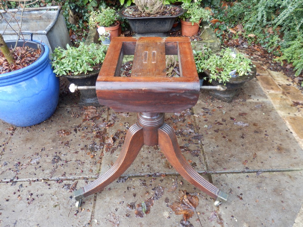 A rectangular mahogany tilt-top table displayed upright on a turned pedestal with splayed reeded legs and brass castors. View II