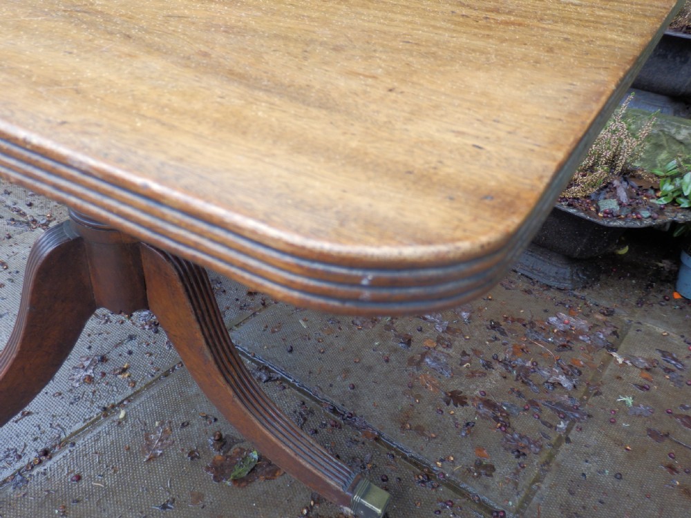 A rectangular mahogany tilt-top table displayed upright on a turned pedestal with splayed reeded legs and brass castors. View X