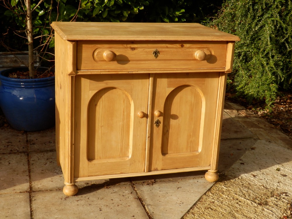 A Victorian pine dresser base with a top drawer, two arched recessed cupboard doors, turned wooden knobs, and brass escutcheons. View III