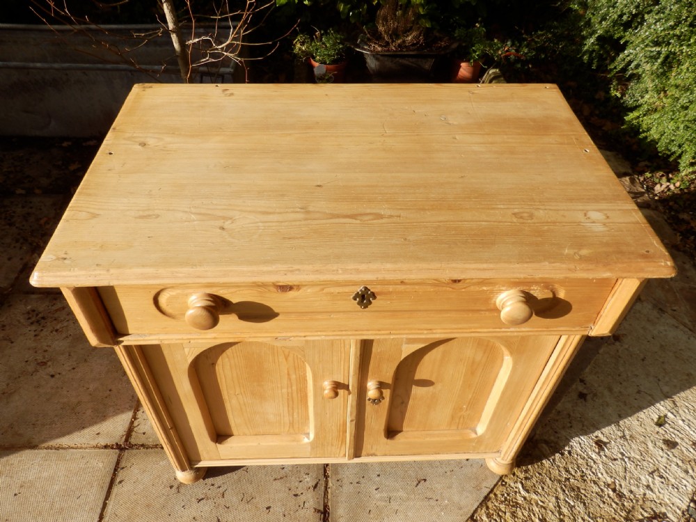 A Victorian pine dresser base with a top drawer, two arched recessed cupboard doors, turned wooden knobs, and brass escutcheons. View V