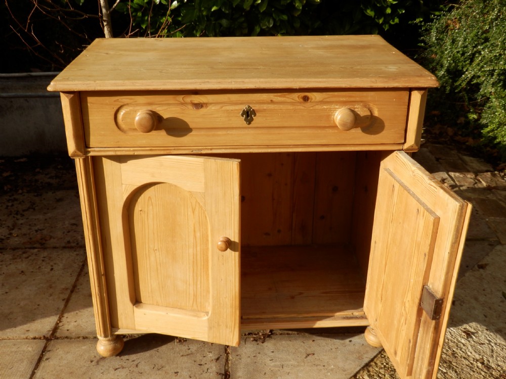 A Victorian pine dresser base with a top drawer, two arched recessed cupboard doors, turned wooden knobs, and brass escutcheons. View VI