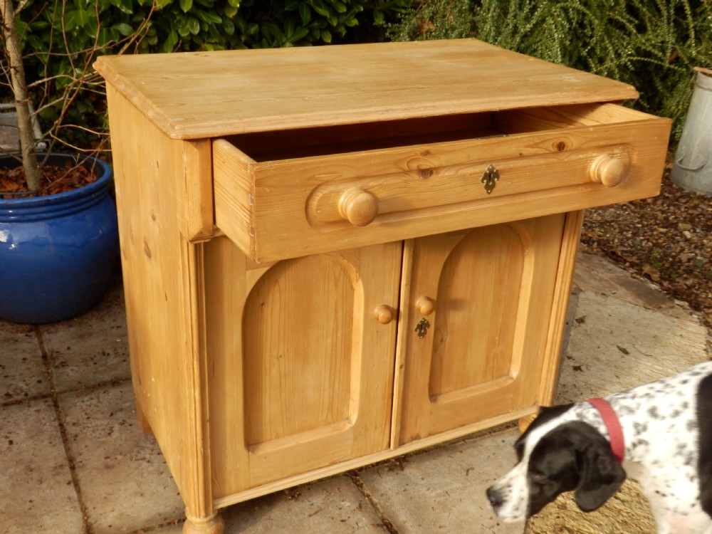 A Victorian pine dresser base with a top drawer, two arched recessed cupboard doors, turned wooden knobs, and brass escutcheons. View VII