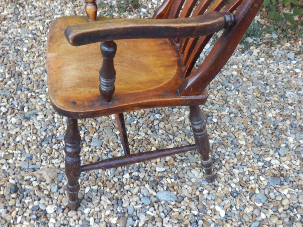 A Victorian wooden Windsor carver armchair featuring a high slat back, turned front legs, curved armrests, and a saddle seat in a dark brown timber finish. View V