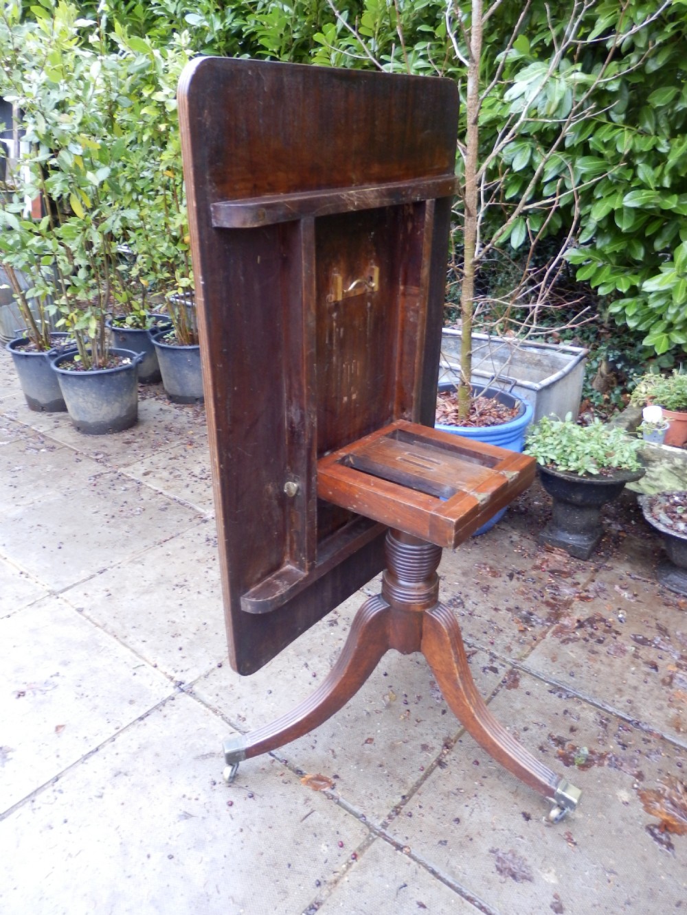 A rectangular mahogany tilt-top table displayed upright on a turned pedestal with splayed reeded legs and brass castors.