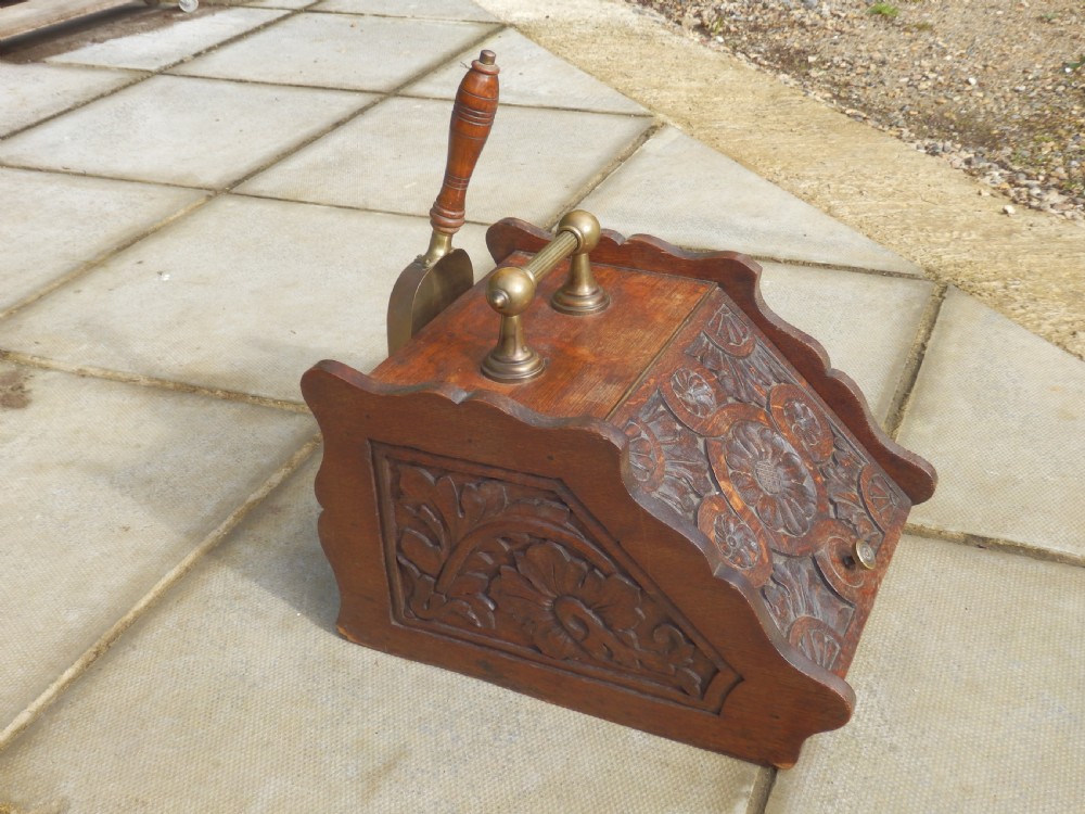 A carved dark oak Arts and Crafts coal purdonium featuring a brass top handle and an integrated shovel stored at the rear. View III