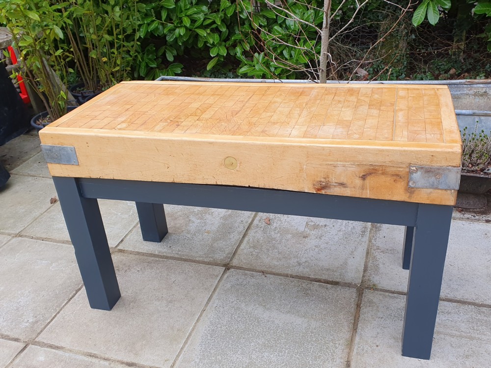 A large rectangular end-grain hardwood butchers block with steel corner brackets set upon a dark grey painted frame.
