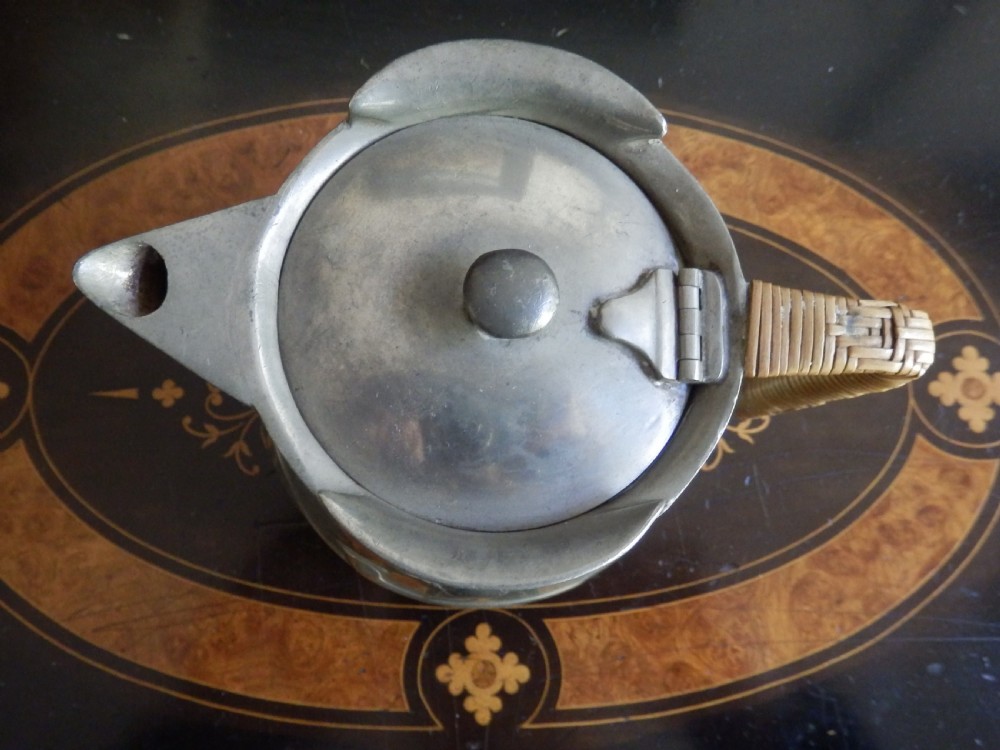 A three-piece pewter tea service consisting of a teapot with a woven cane handle, a sugar bowl, and a cream jug featuring relief plant motifs. View IV
