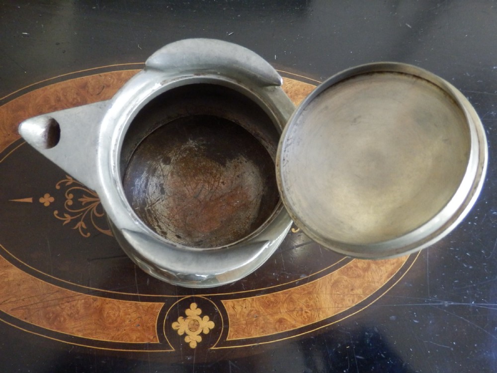 A three-piece pewter tea service consisting of a teapot with a woven cane handle, a sugar bowl, and a cream jug featuring relief plant motifs. View V