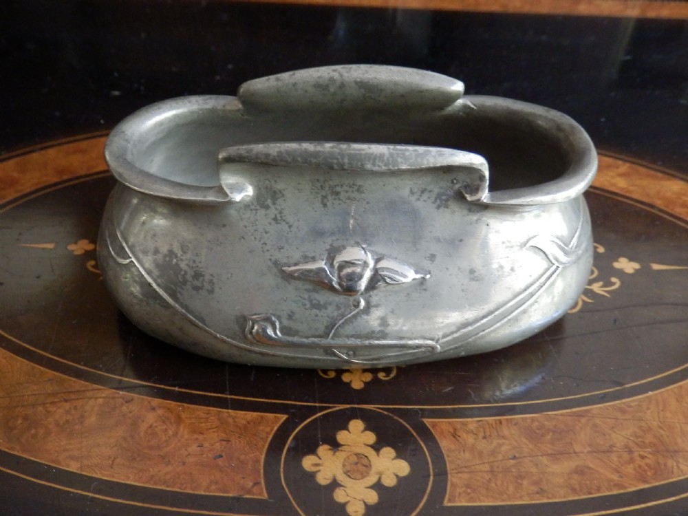 A three-piece pewter tea service consisting of a teapot with a woven cane handle, a sugar bowl, and a cream jug featuring relief plant motifs. View VIII
