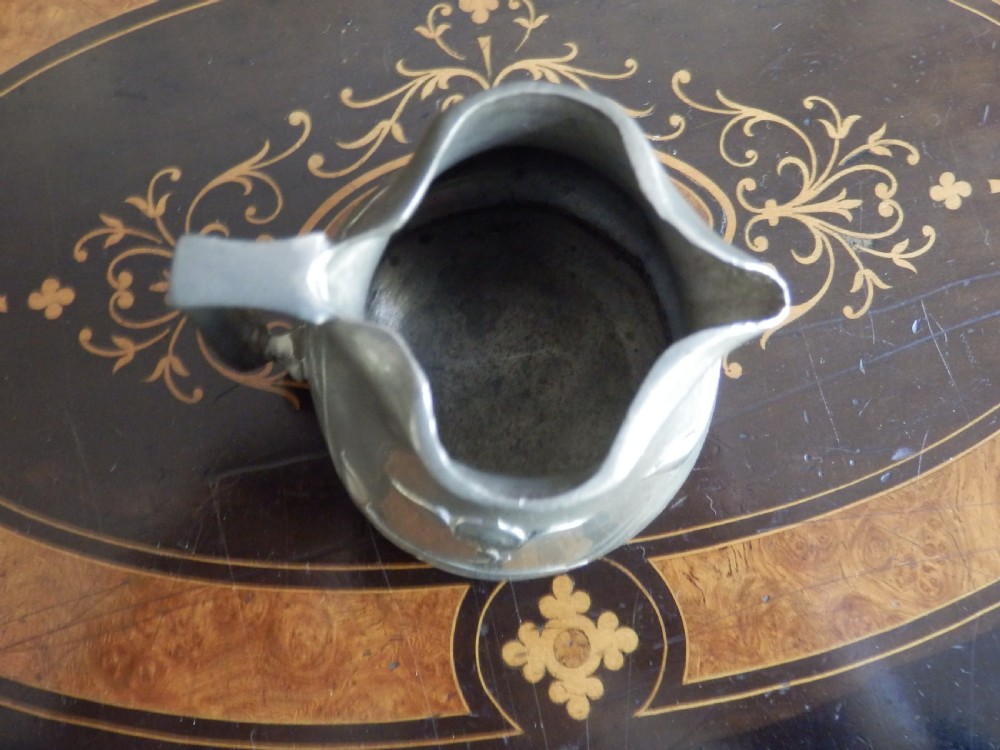 A three-piece pewter tea service consisting of a teapot with a woven cane handle, a sugar bowl, and a cream jug featuring relief plant motifs. View XII