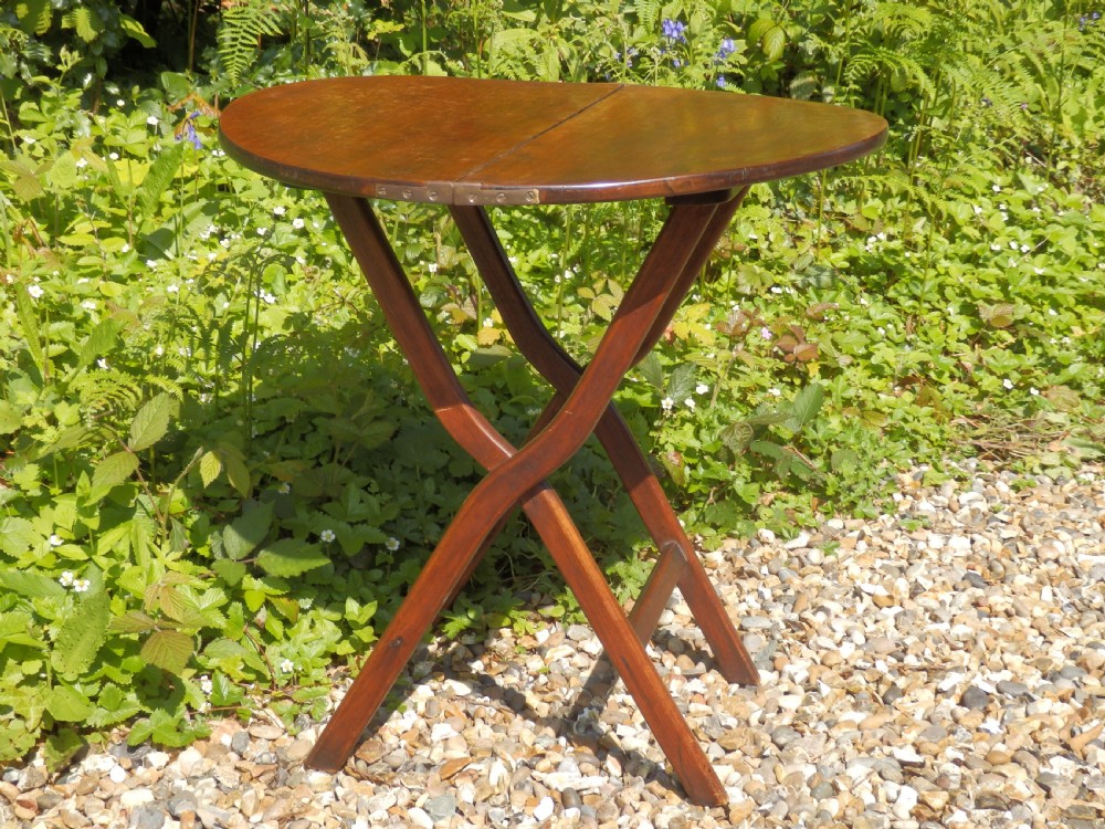 A Victorian mahogany folding coaching table featuring a circular top supported by an X-frame leg assembly with brass rim hinges.