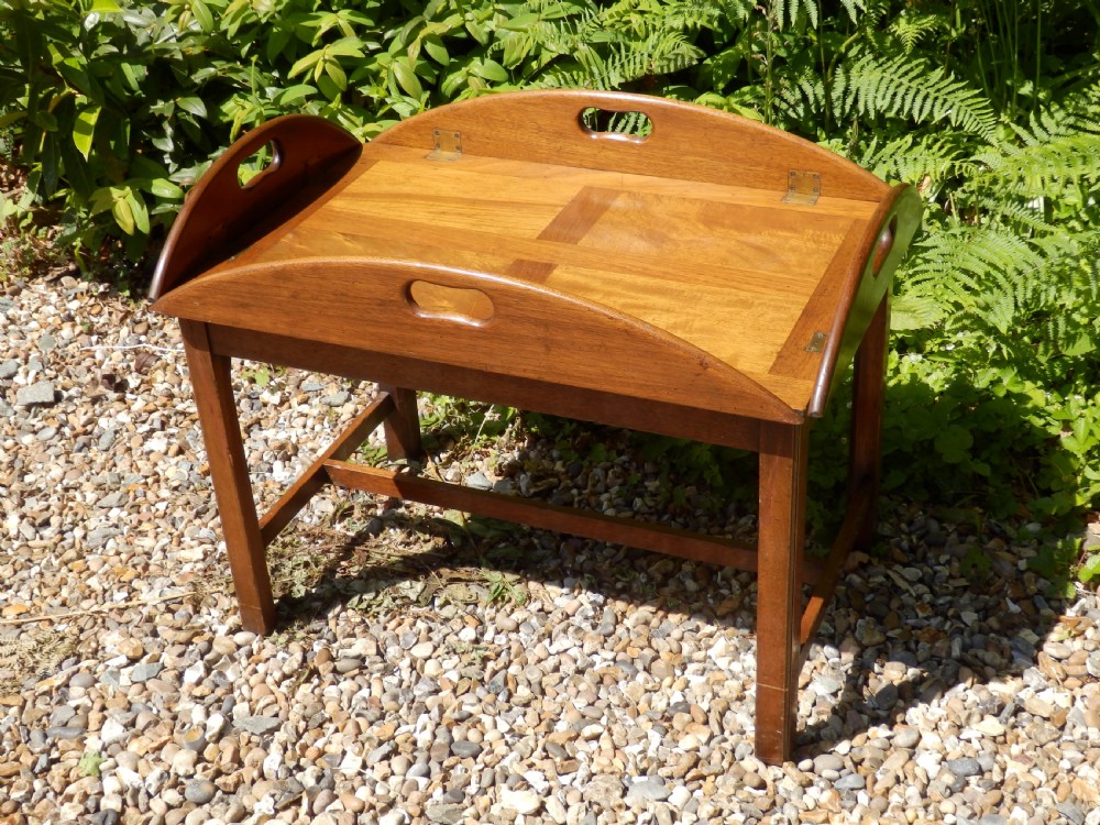 A Victorian mahogany butlers tray featuring four hinged curved sides with cut-out handles, set upon a low wooden stand.