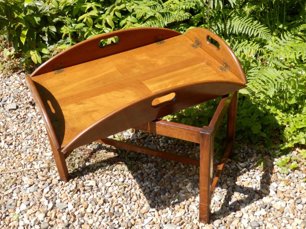 A Victorian mahogany butlers tray featuring four hinged curved sides with cut-out handles, set upon a low wooden stand. View II