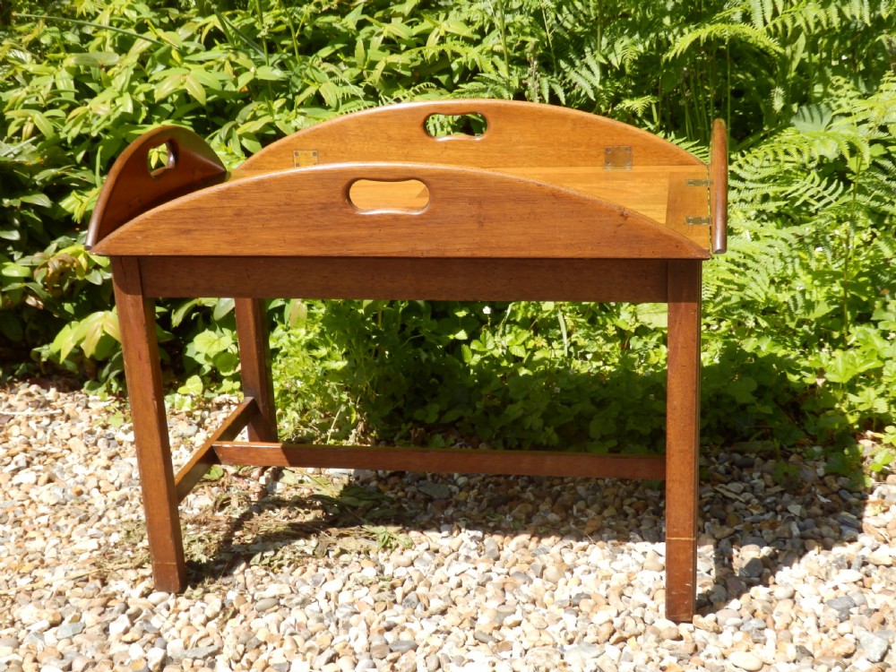 A Victorian mahogany butlers tray featuring four hinged curved sides with cut-out handles, set upon a low wooden stand. View IV