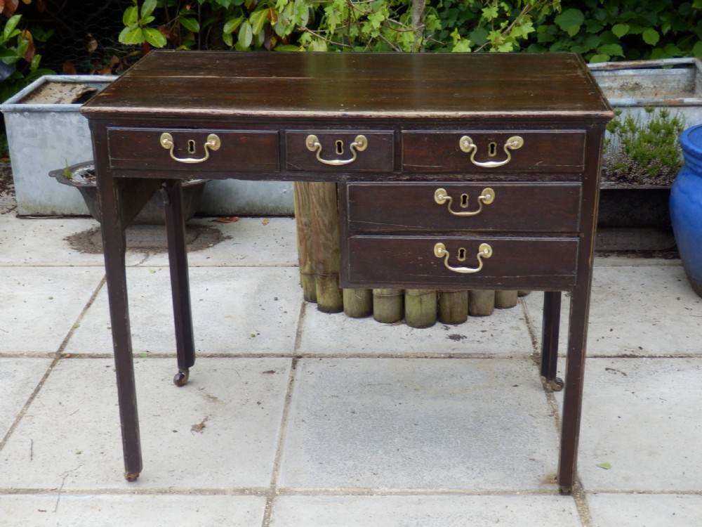 A Victorian dark wood writing desk featuring five drawers with brass swan-neck handles and brass keyhole escutcheons, supported by slender legs on small castors.