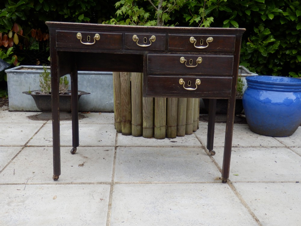 A Victorian dark wood writing desk featuring five drawers with brass swan-neck handles and brass keyhole escutcheons, supported by slender legs on small castors. View III