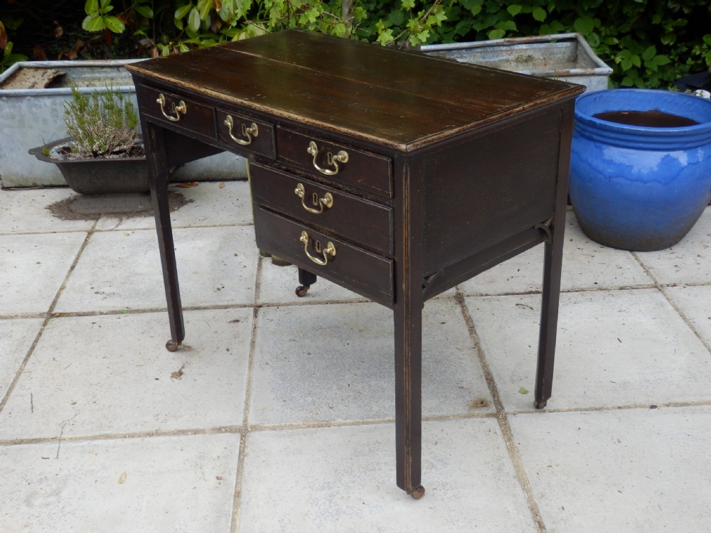 A Victorian dark wood writing desk featuring five drawers with brass swan-neck handles and brass keyhole escutcheons, supported by slender legs on small castors. View V