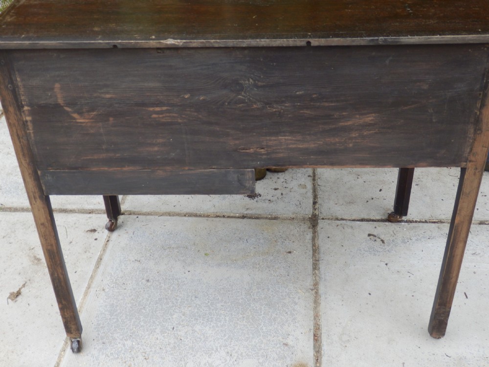 A Victorian dark wood writing desk featuring five drawers with brass swan-neck handles and brass keyhole escutcheons, supported by slender legs on small castors. View VI