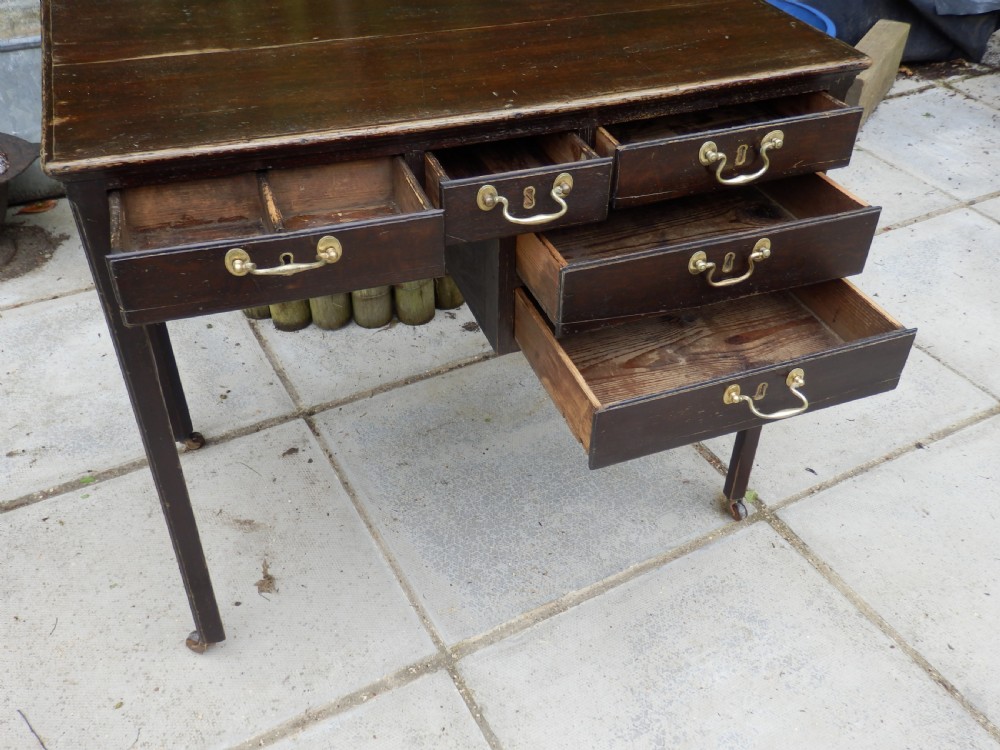 A Victorian dark wood writing desk featuring five drawers with brass swan-neck handles and brass keyhole escutcheons, supported by slender legs on small castors. View IX