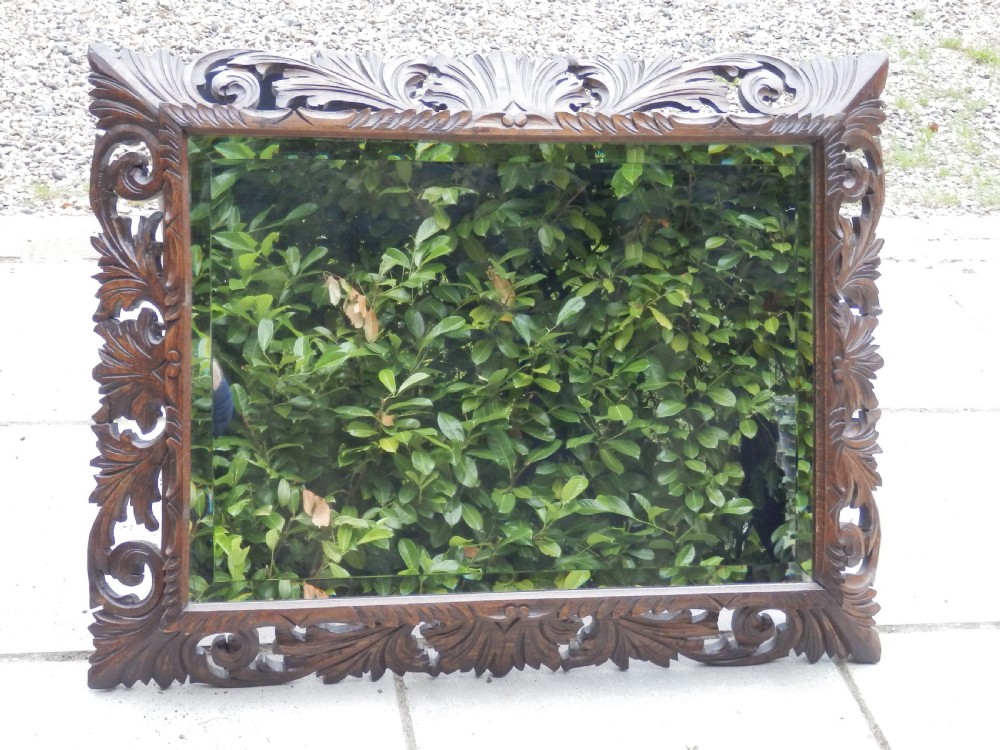 An Edwardian rectangular wall mirror set within a dark oak frame deeply carved with acanthus leaves and scrollwork motifs.