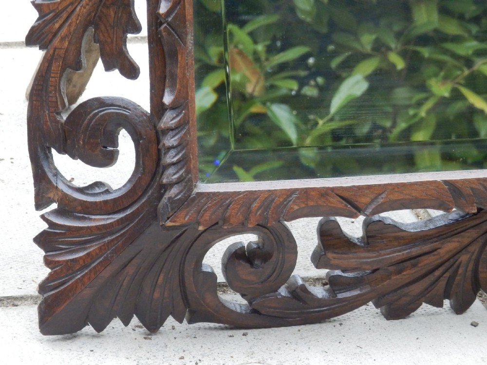 An Edwardian rectangular wall mirror set within a dark oak frame deeply carved with acanthus leaves and scrollwork motifs. View III