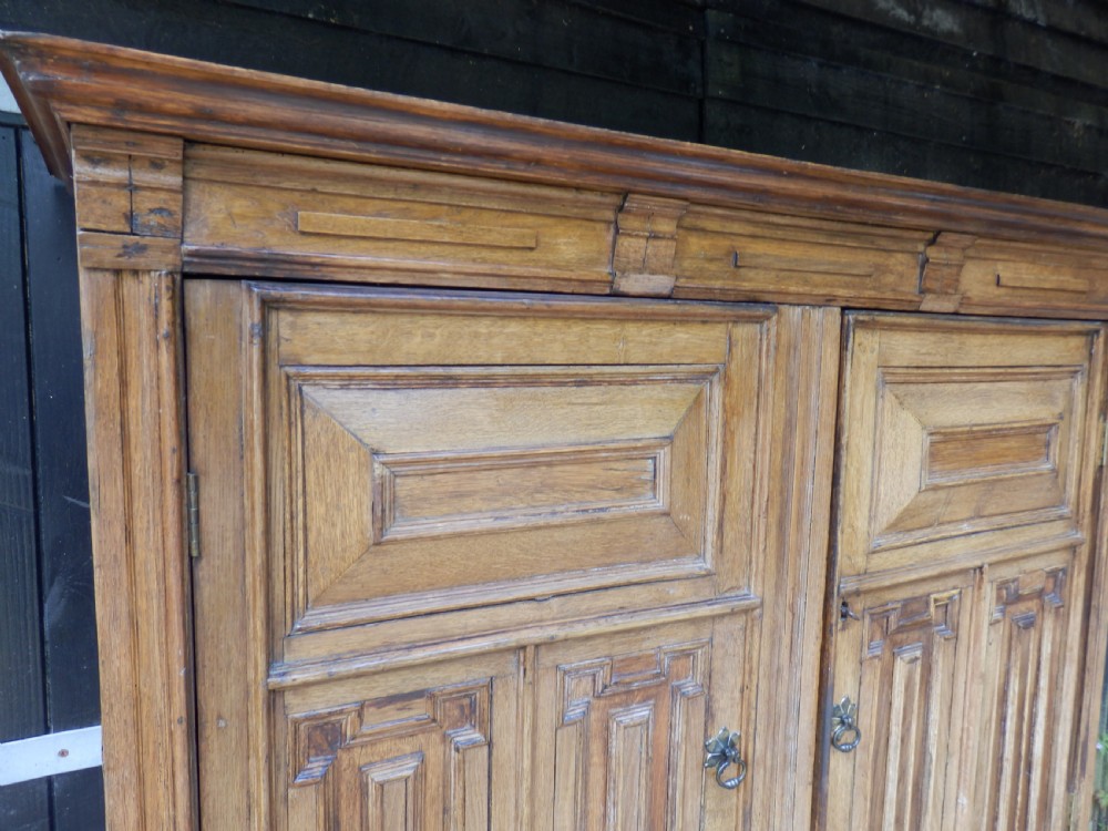 An 18th-century solid oak hall cupboard featuring double doors with geometric fielded panelling, lower drawers, and a stepped top cornice. View V