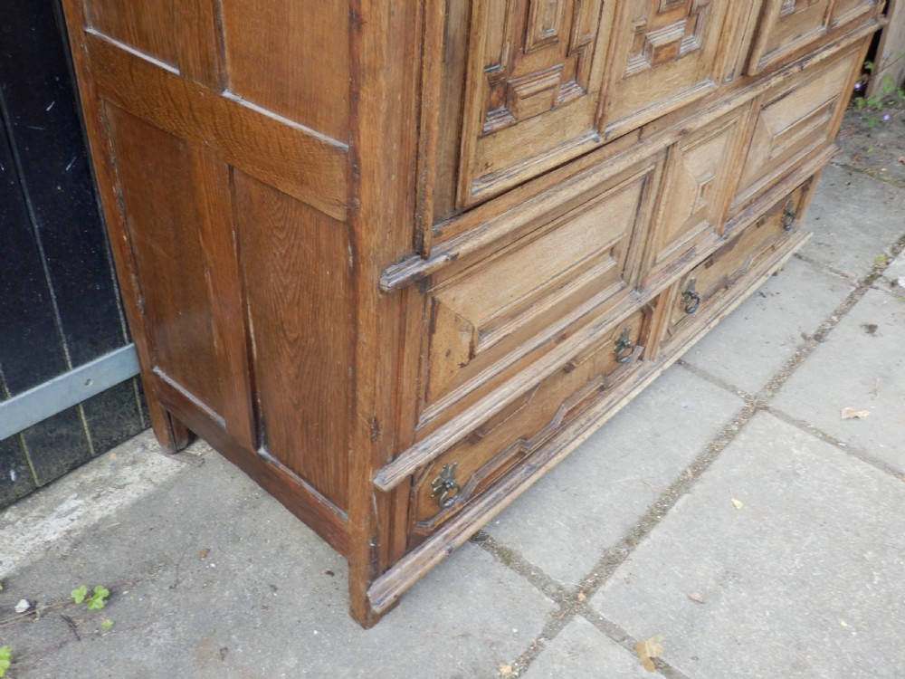 An 18th-century solid oak hall cupboard featuring double doors with geometric fielded panelling, lower drawers, and a stepped top cornice. View VIII