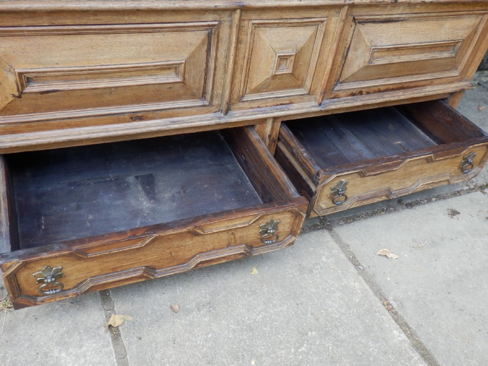 An 18th-century solid oak hall cupboard featuring double doors with geometric fielded panelling, lower drawers, and a stepped top cornice. View IX